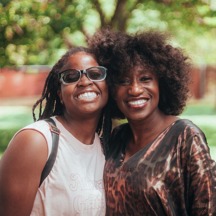 Two women joyfully embrace, smiling brightly in a sunny park setting, capturing a moment of friendship and happiness.